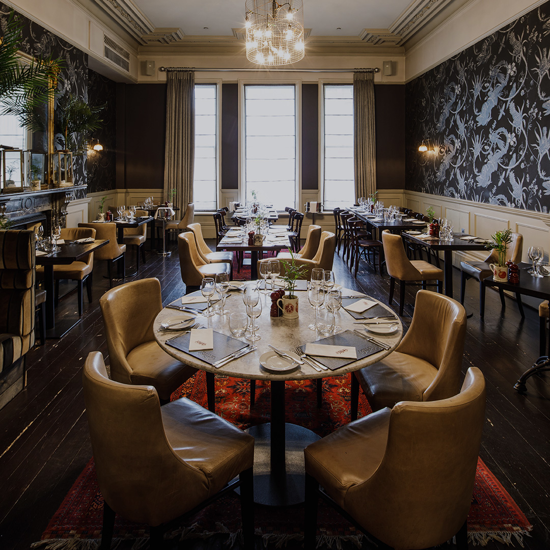 A large brasserie with patterned wallpaper, elegant rugs, and a large white marble table