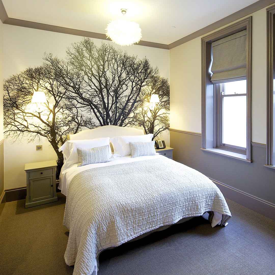 King-size bed with luxury bedding in front of a tree-themed feature wall