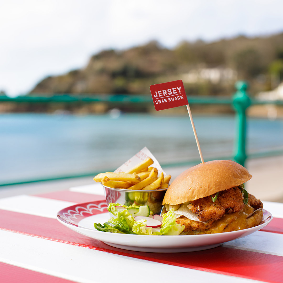 A burger on an al fresco table, in front of a view of the beach