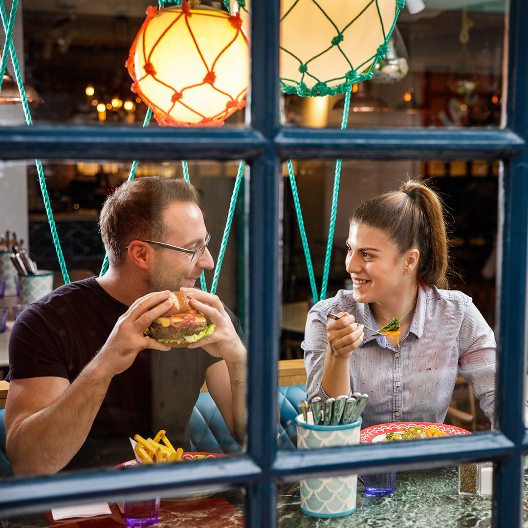 A male and female chat and laugh while eating food in a nautical-themed booth