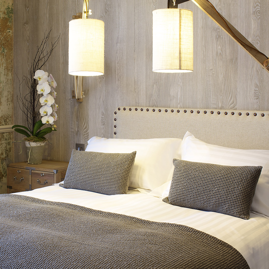 Elegant bed with textured bedding, hanging light fixtures, and pretty orchid