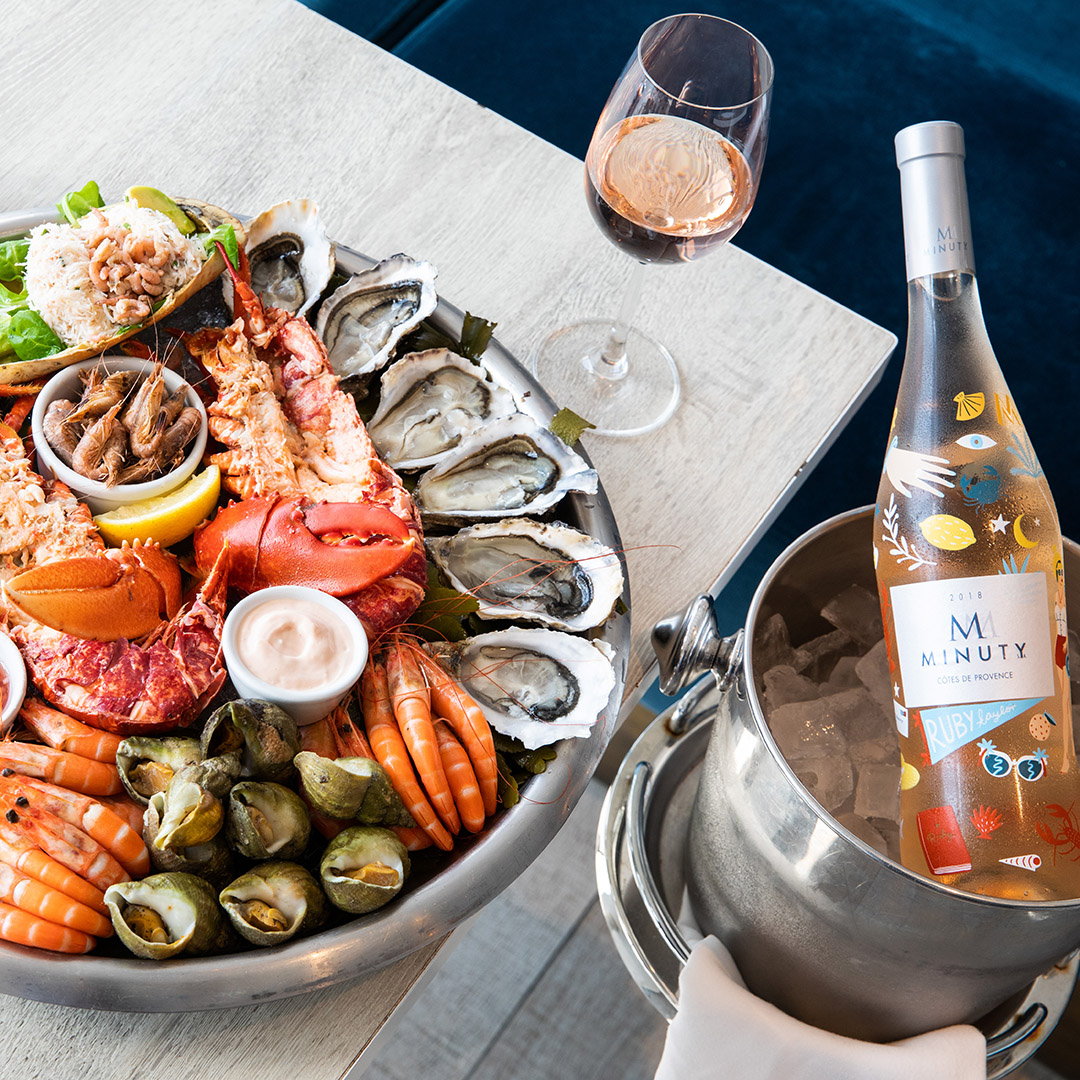 A bottle of wine beside a platter full of oysters, lobster, and other local seafood